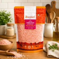 Standard Store Himalayan Crystal Salt pouch placed on a kitchen table with pink salt crystals in wooden bowls and cooking background.